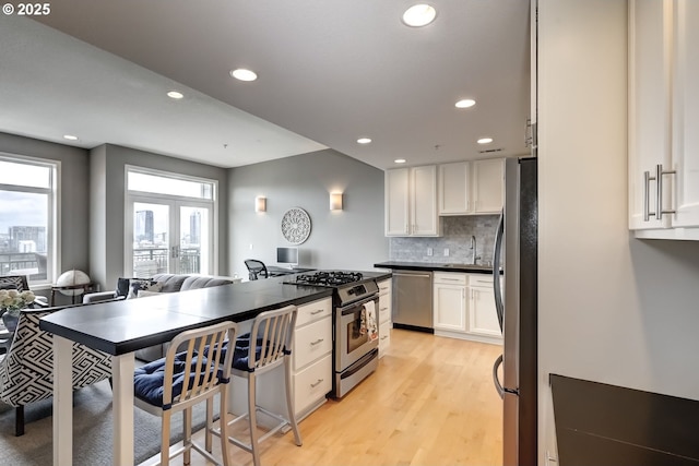 kitchen with white cabinets, dark countertops, stainless steel appliances, light wood-type flooring, and a sink