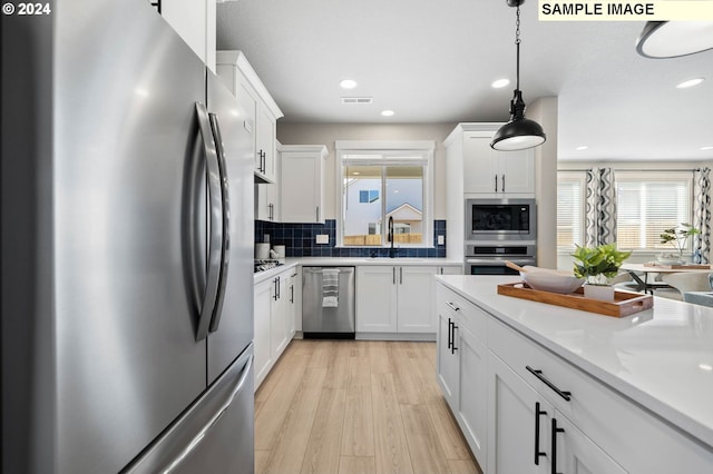 kitchen featuring white cabinetry, hanging light fixtures, appliances with stainless steel finishes, light hardwood / wood-style floors, and backsplash