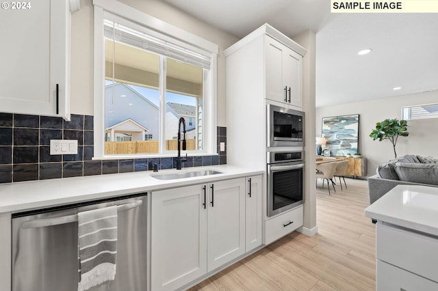 kitchen with appliances with stainless steel finishes, white cabinetry, sink, decorative backsplash, and light hardwood / wood-style flooring