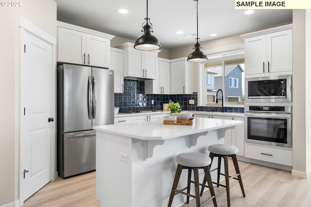 kitchen featuring stainless steel appliances, white cabinetry, a center island, and decorative light fixtures