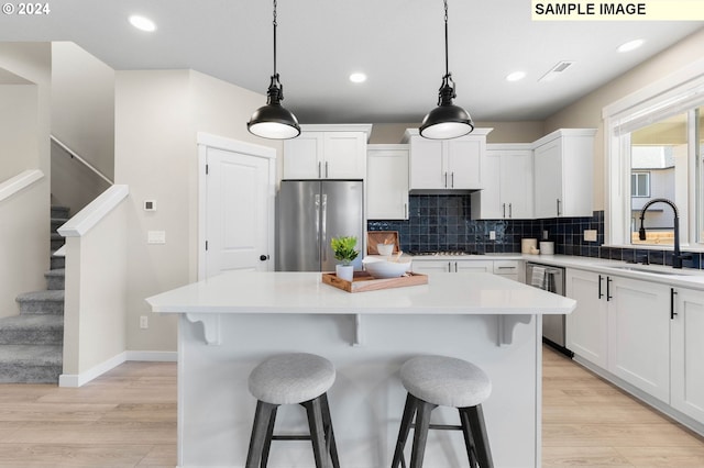 kitchen featuring sink, appliances with stainless steel finishes, white cabinets, a kitchen island, and decorative light fixtures