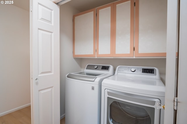 laundry room featuring washer and clothes dryer, cabinet space, baseboards, and wood finished floors