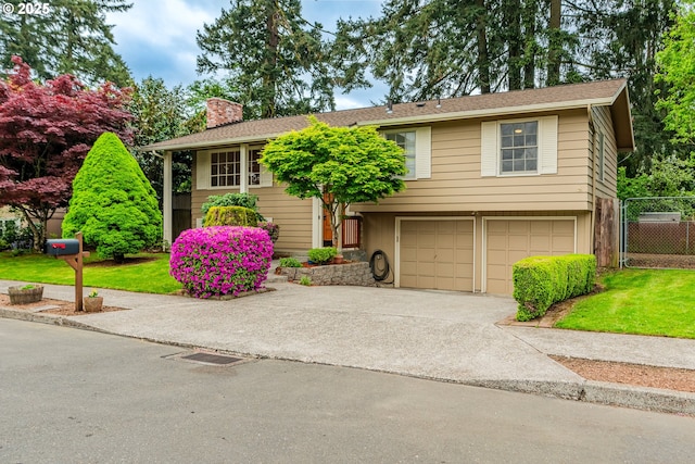 split foyer home with fence, a garage, a front yard, a chimney, and driveway