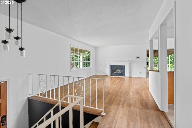 corridor featuring a textured ceiling, baseboards, an upstairs landing, and light wood-style flooring
