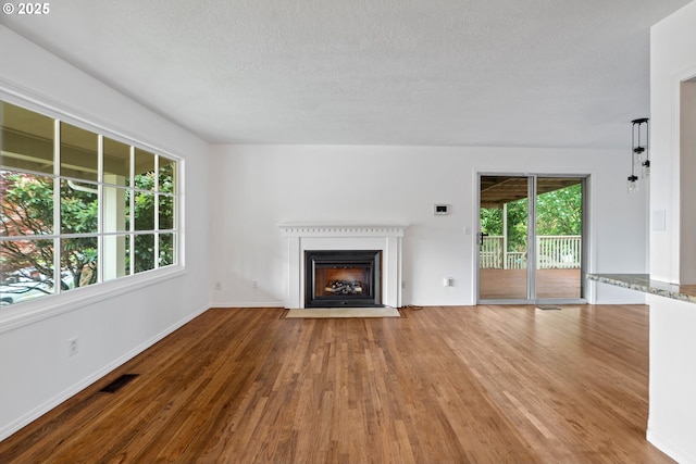 unfurnished living room with a textured ceiling, visible vents, a fireplace with flush hearth, wood finished floors, and baseboards