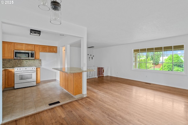 kitchen featuring tasteful backsplash, brown cabinets, stainless steel microwave, white range with electric stovetop, and light wood-style flooring