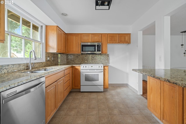 kitchen with light stone countertops, tasteful backsplash, a sink, appliances with stainless steel finishes, and light tile patterned floors