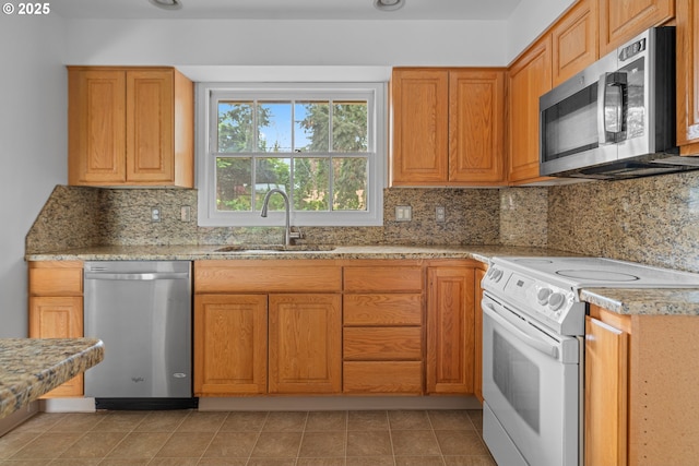 kitchen with decorative backsplash, light stone counters, a sink, appliances with stainless steel finishes, and light tile patterned floors