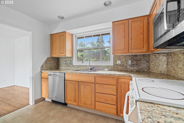 kitchen featuring brown cabinets, appliances with stainless steel finishes, light stone counters, a sink, and backsplash