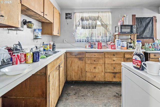 kitchen featuring black microwave, light countertops, washer / dryer, a sink, and concrete floors