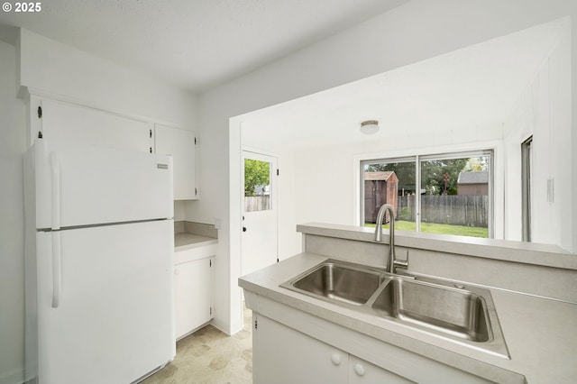 kitchen with freestanding refrigerator, a sink, white cabinets, and light countertops