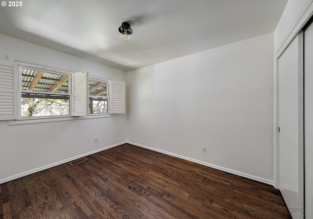 unfurnished bedroom featuring baseboards, dark wood-type flooring, visible vents, and a closet