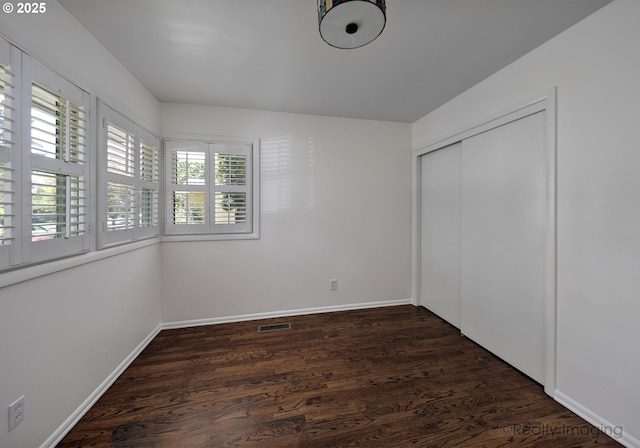 unfurnished bedroom with baseboards, a closet, dark wood-style flooring, and visible vents