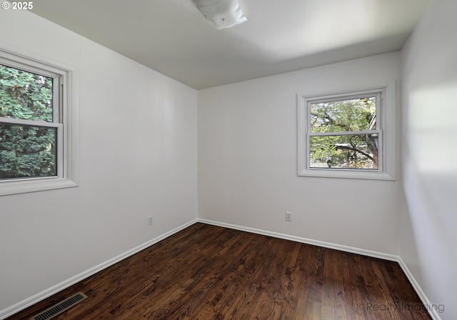 spare room featuring visible vents, baseboards, and dark wood-style floors