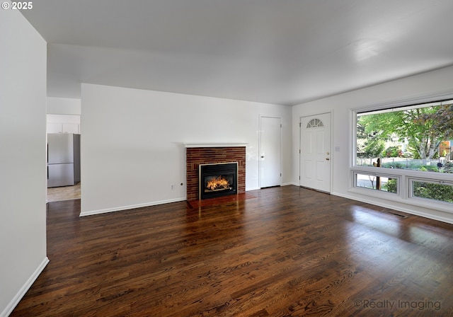unfurnished living room with a brick fireplace, baseboards, visible vents, and dark wood-type flooring