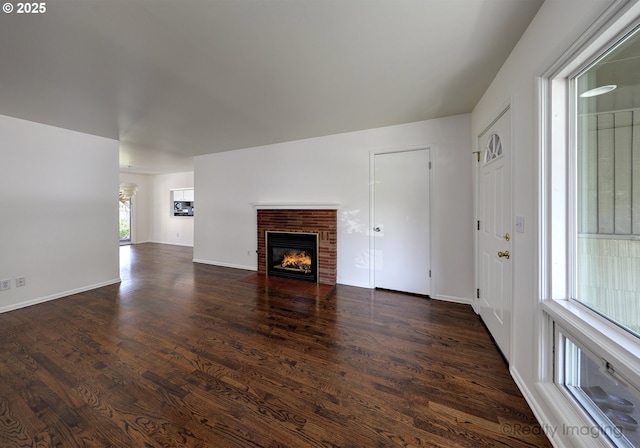 unfurnished living room with baseboards, a brick fireplace, and dark wood finished floors