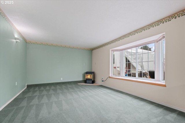 unfurnished room featuring a wood stove, baseboards, and carpet floors