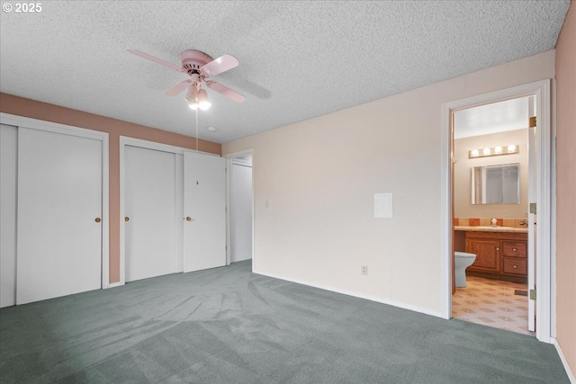 unfurnished bedroom featuring multiple closets, carpet flooring, ensuite bath, a textured ceiling, and a ceiling fan