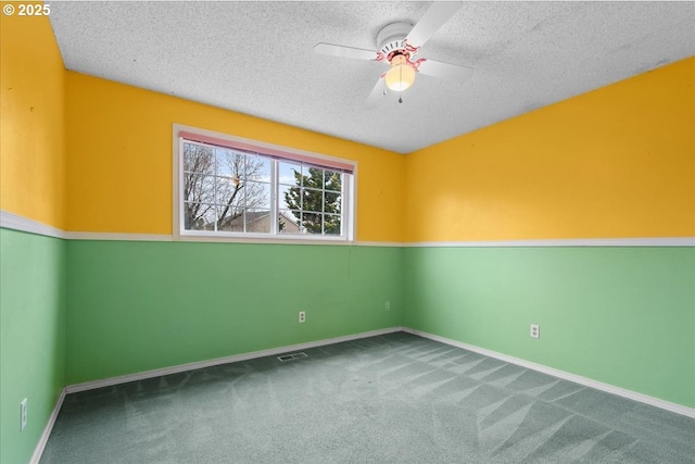 carpeted spare room with visible vents, a ceiling fan, baseboards, and a textured ceiling