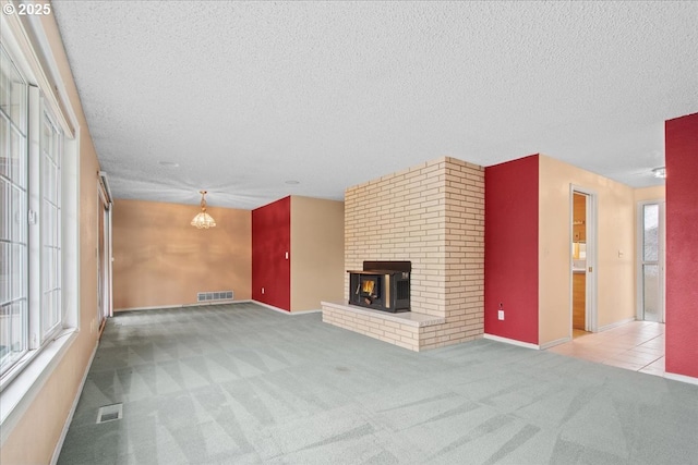 unfurnished living room featuring visible vents, carpet floors, an inviting chandelier, a textured ceiling, and a brick fireplace