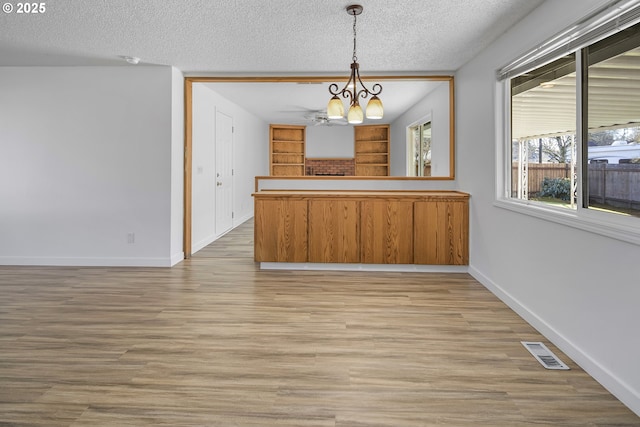 unfurnished dining area with an inviting chandelier, light hardwood / wood-style flooring, and a textured ceiling