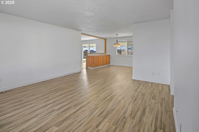 unfurnished living room featuring an inviting chandelier, light hardwood / wood-style flooring, and a textured ceiling