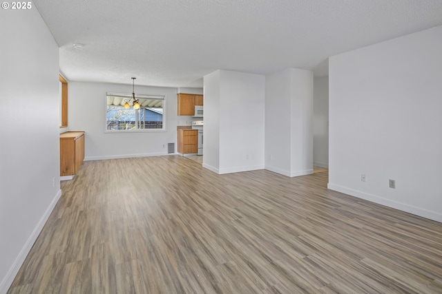 unfurnished living room with an inviting chandelier, a textured ceiling, and light hardwood / wood-style flooring