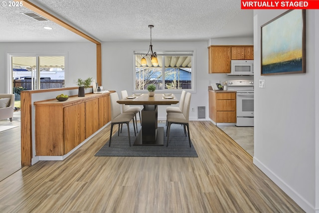 dining space featuring an inviting chandelier, light hardwood / wood-style floors, and a textured ceiling