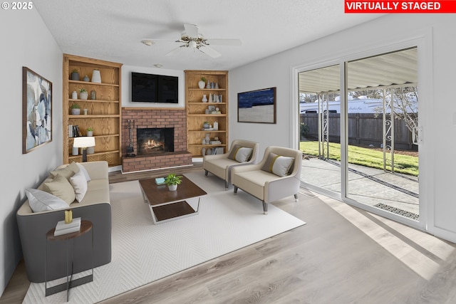 living room with built in features, ceiling fan, light hardwood / wood-style floors, a brick fireplace, and a textured ceiling