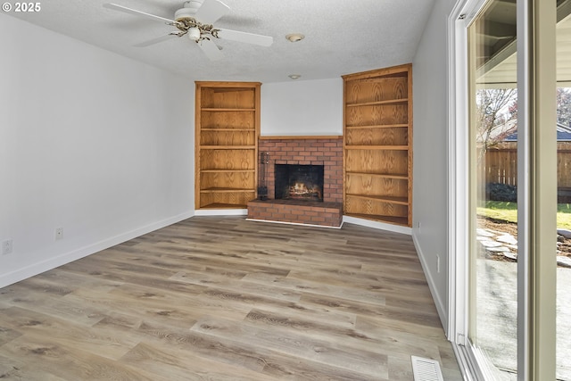 unfurnished living room featuring hardwood / wood-style floors, a fireplace, ceiling fan, a textured ceiling, and built in shelves