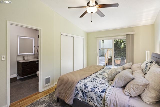 bedroom featuring wood finished floors, vaulted ceiling, a closet, ensuite bath, and baseboards