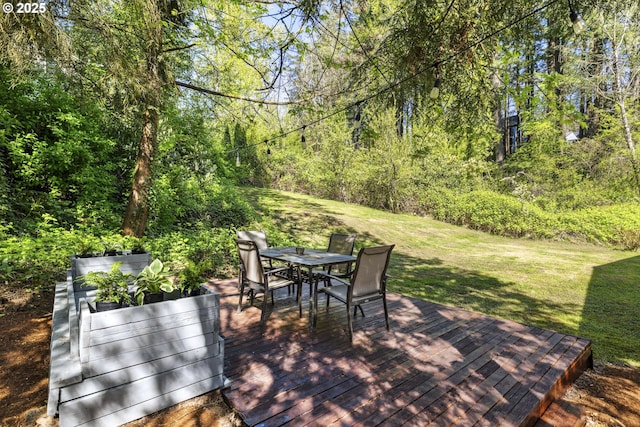 wooden terrace featuring outdoor dining space, a lawn, and a wooded view