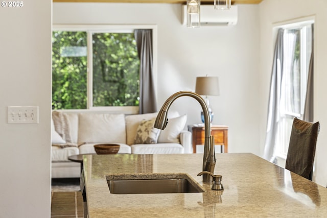 kitchen view of a sink, a wall unit AC, and light stone counters