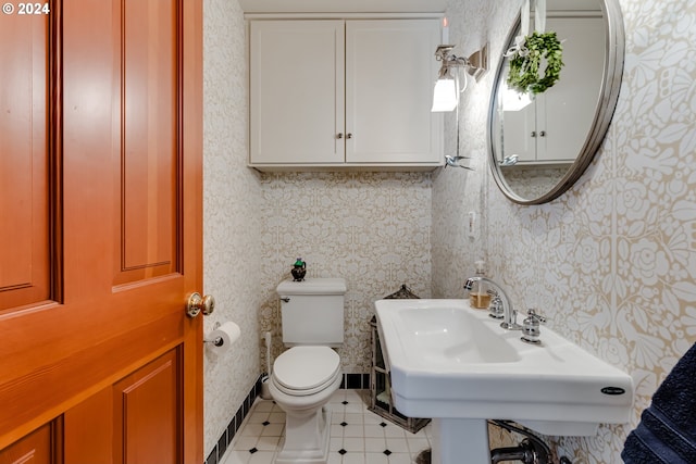 half bathroom with a sink, toilet, tile patterned flooring, and wallpapered walls