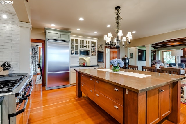 kitchen featuring decorative columns, built in appliances, tasteful backsplash, a center island, and light wood-style flooring