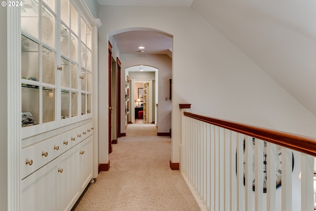 hall with arched walkways, baseboards, vaulted ceiling, and light carpet