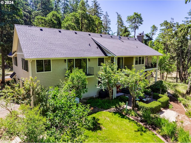 back of property with a shingled roof, a yard, and a chimney