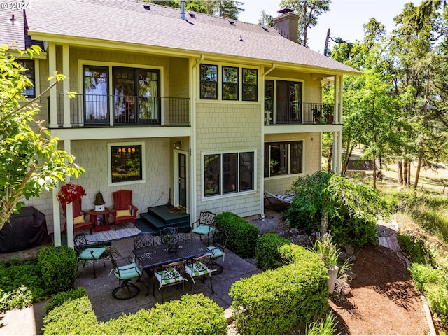 back of property featuring a balcony, a chimney, a shingled roof, and a patio