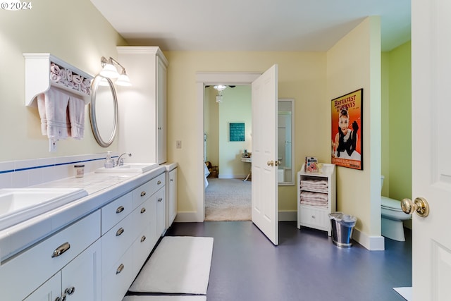 bathroom featuring toilet, a sink, concrete floors, baseboards, and double vanity