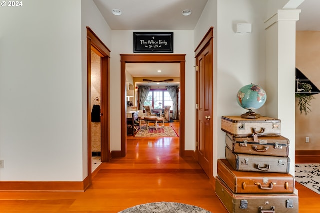 hallway with baseboards, wood finished floors, and decorative columns