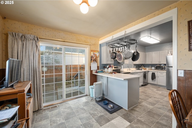 kitchen with radiator heating unit, stainless steel appliances, white cabinets, decorative light fixtures, and kitchen peninsula