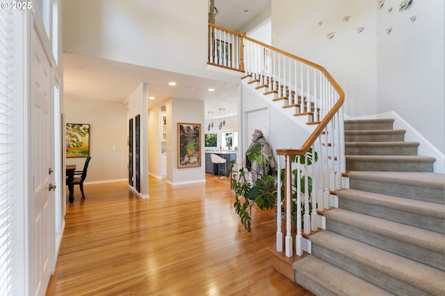 entrance foyer featuring stairway, light wood-style floors, a high ceiling, and baseboards