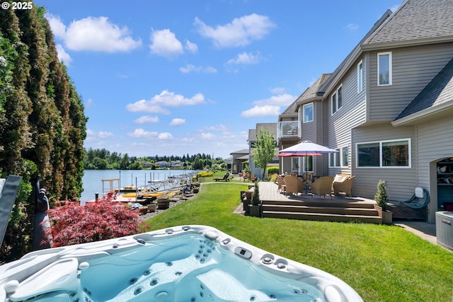 view of grassy yard featuring a hot tub, a deck with water view, and outdoor dining space
