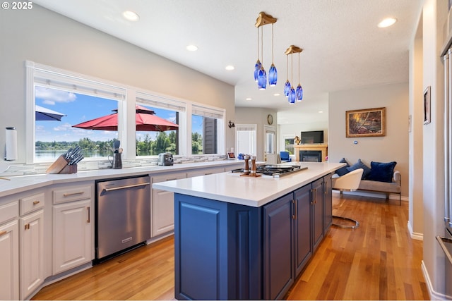 kitchen featuring stainless steel appliances, white cabinetry, a glass covered fireplace, light countertops, and a center island
