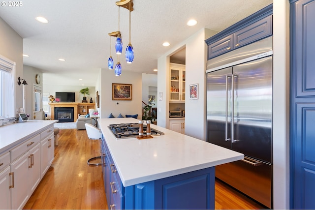 kitchen featuring appliances with stainless steel finishes, light wood-type flooring, blue cabinetry, a center island, and recessed lighting