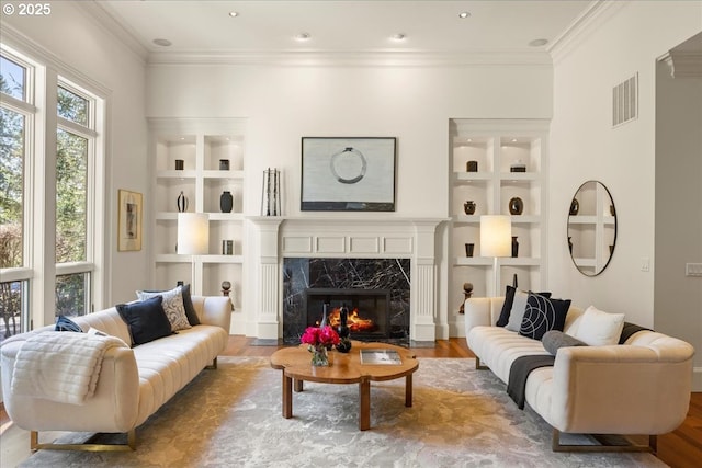 living room with visible vents, crown molding, built in features, a fireplace, and wood finished floors