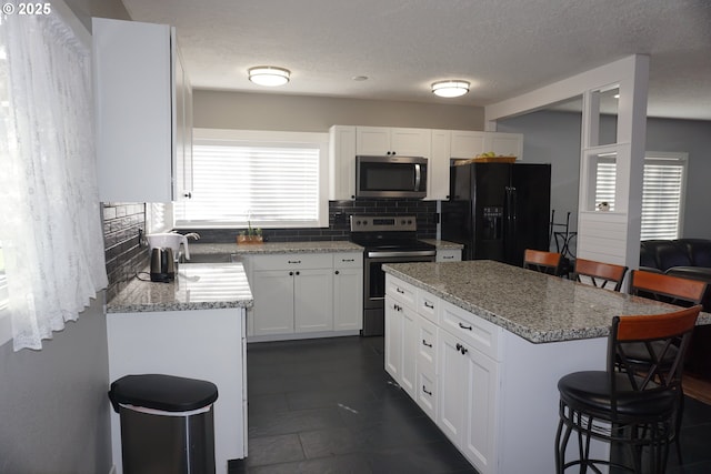 kitchen featuring light stone counters, tasteful backsplash, appliances with stainless steel finishes, white cabinetry, and a kitchen breakfast bar