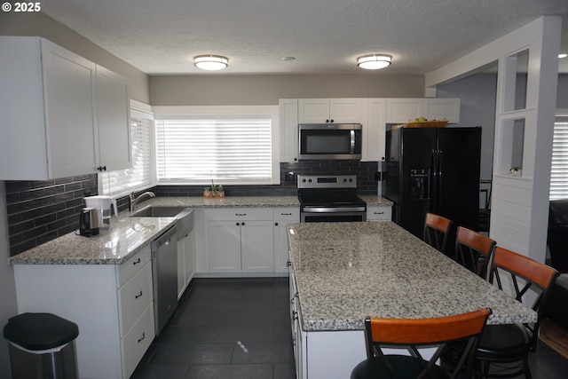 kitchen with stainless steel appliances, a kitchen island, a sink, white cabinetry, and a kitchen bar