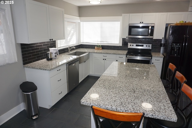 kitchen featuring light stone counters, decorative backsplash, appliances with stainless steel finishes, white cabinetry, and a sink