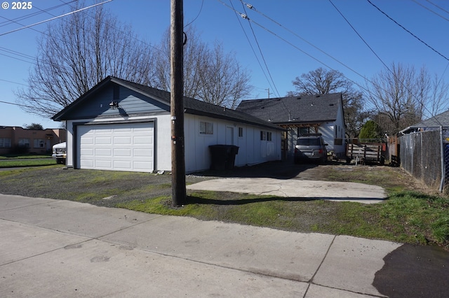 view of side of property with board and batten siding, aphalt driveway, a detached garage, and fence